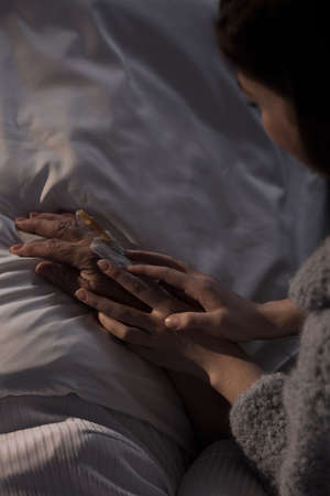 Young supportive woman holding her sick mother's hand