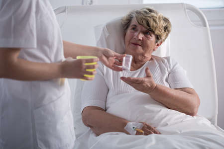 Nurse giving medications to older sick woman