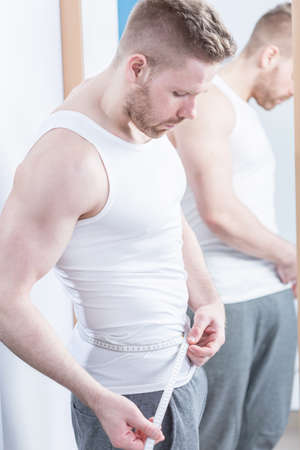 Muscular fit man checking his waist circumferenceの写真素材