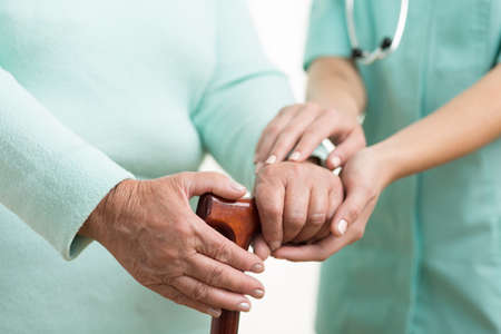Close up of carer helping disabled female with walking stickの写真素材