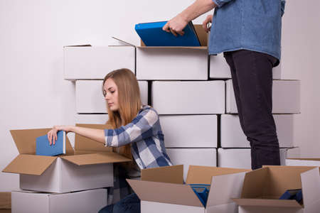 Young couple hiding the books to cartons during moving outの写真素材