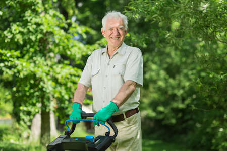 Senior man with lawn mower in the gardenの写真素材