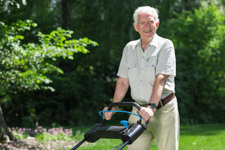 Smiling retiree cutting grass with lawn mowerの写真素材