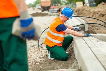 Young male construction worker putting paving stones