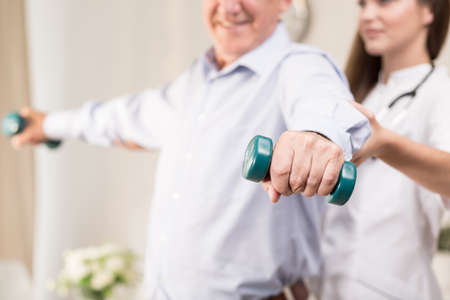 Retiree training with dumbbells assisted by young physiotherapistの写真素材