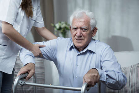 Physiotherapist helping disabled senior man with standing