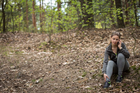 Jogging woman with sprinkled ankle calling for helpの写真素材