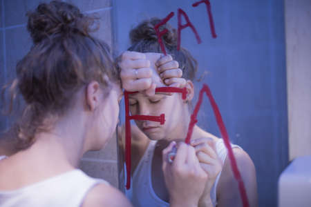Picture of bulimic girl and red writing fat on mirrorの写真素材