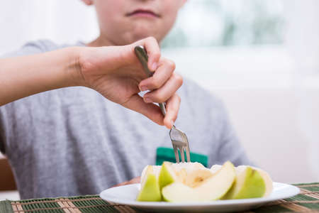 Close-up of displeased boy eating healthy appleの写真素材