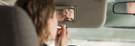 Woman is puting the lipstick on during driving