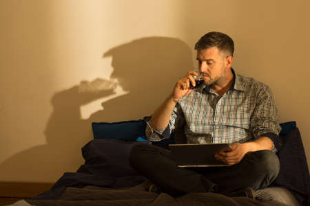 Man using laptop and drinking wine at eveningの写真素材