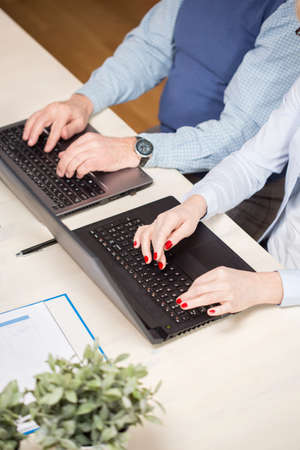 Close-up of two elderly businesspeople writing on computersの写真素材