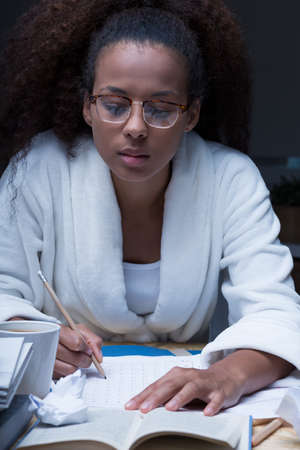 Forgetful female student doing homework at nightの写真素材