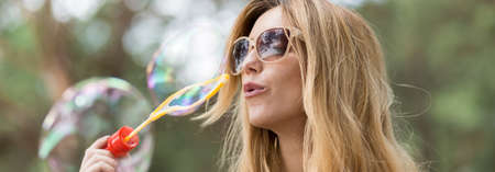 Panoramic picture of young girl in sunglasses blowing bubbles
