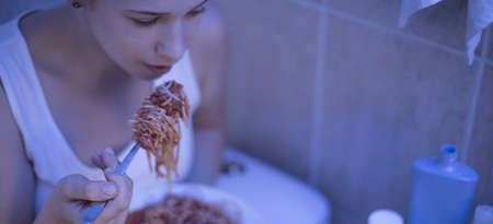 Young girl with eating disorder is stuffing herself with spaghettiの写真素材