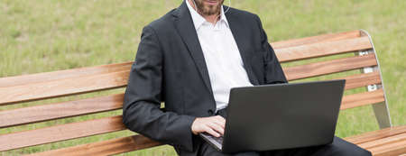Panorama of modern businessman sitting with laptop in the parkの写真素材