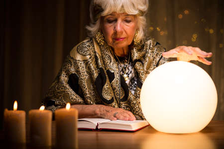 Old fortune teller is learning how to use crystal ballの写真素材
