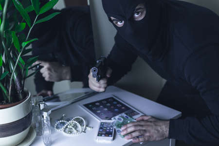 Dangerous robber with handgun taking money and electronics