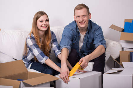 Young couple is taping the box during moving outの写真素材