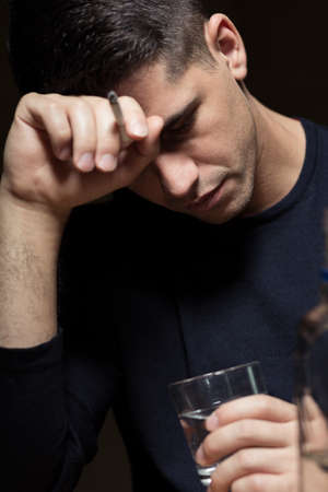 Desperate man abusing alcohol and smoking a cigaretteの写真素材