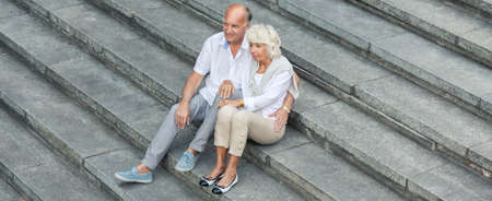 Elder couple is sitting together on the stairsの写真素材