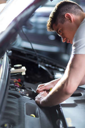 Portrait of young busy auto mechanic fixing carの写真素材