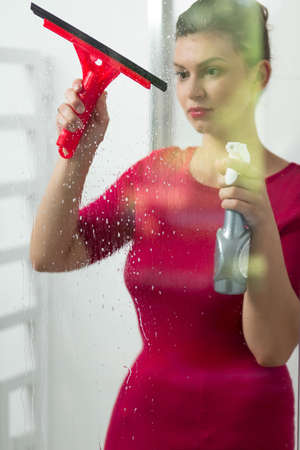 Perfect housewife using squeegee to wash windowの写真素材