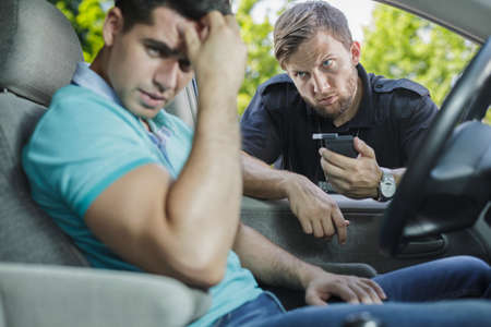 Angry police officer with breathalyser and young male driver