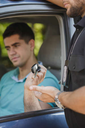 Police officer taking the car keys from young drunk manの写真素材