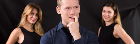 Young man choosing between two beautiful womenの写真素材