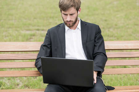 Young man sitting on bench with laptop on kneesの写真素材