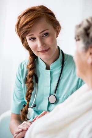 Photo of female doctor with stethoscope during home visitの写真素材