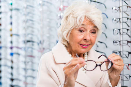 Senior woman trying on eyeglasses in optician storeの写真素材