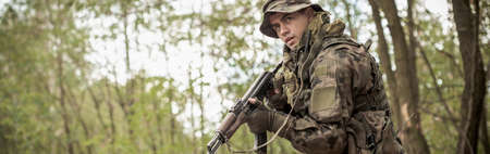 Handsome uniformed soldier with equipment alone in forestの写真素材