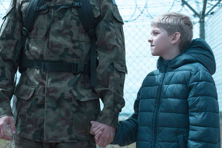 Little boy is holding his father soldier handの写真素材
