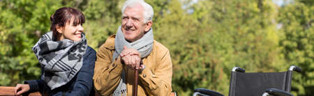 Disabled man with walking stick and wheelchair in parkの写真素材