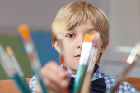 Portrait of little artist hiding behind paintbrushesの写真素材