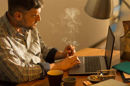 Image of bearded male sitting at laptop with cigaretteの写真素材