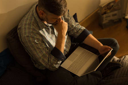 Photo of serious guy sitting crossed legg with his laptopの写真素材