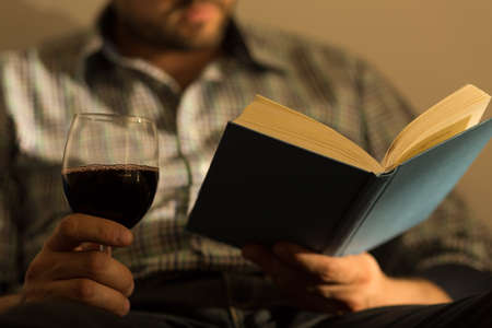 Close up of male hands holding book and glass of wineの写真素材