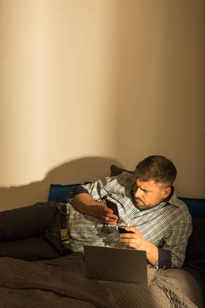 Photo of worried man lying in messy bed with computer