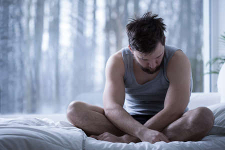 Depressed insomniac man sitting on bed in daylightの写真素材