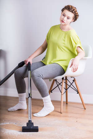 Image of exhausted housewife with vacuum resting on chairの写真素材