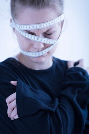 Young anorexic woman wrapped in tape measureの写真素材