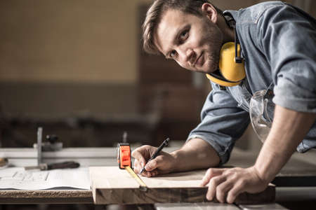 Photo of handsome carpenter measuring wooden board