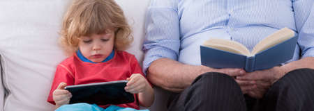Little grandson with tablet and grandfather with book