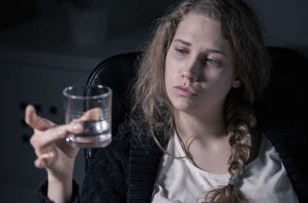 Alcoholic woman is looking at the glass with vodkaの写真素材