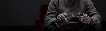 Male hand holding bottle of alcohol and glassの写真素材