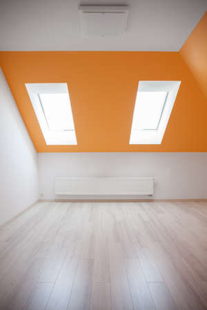 Empty attic room with orange sloped ceilingの写真素材