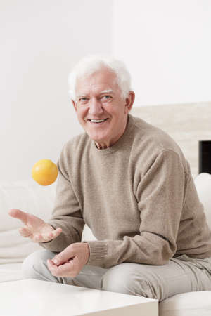 Happy old man is tossing an orangeの写真素材